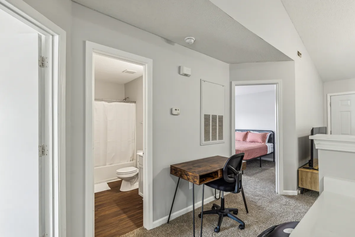 A cozy multi-functional interior space featuring a wooden desk and chair, a television, and access to both the bathroom and the bedroom. The scene highlights a tidy, well-equipped environment ideal for productivity or relaxation, illustrating modern conveniences like high-speed Wi-Fi and a comfortable work setup.