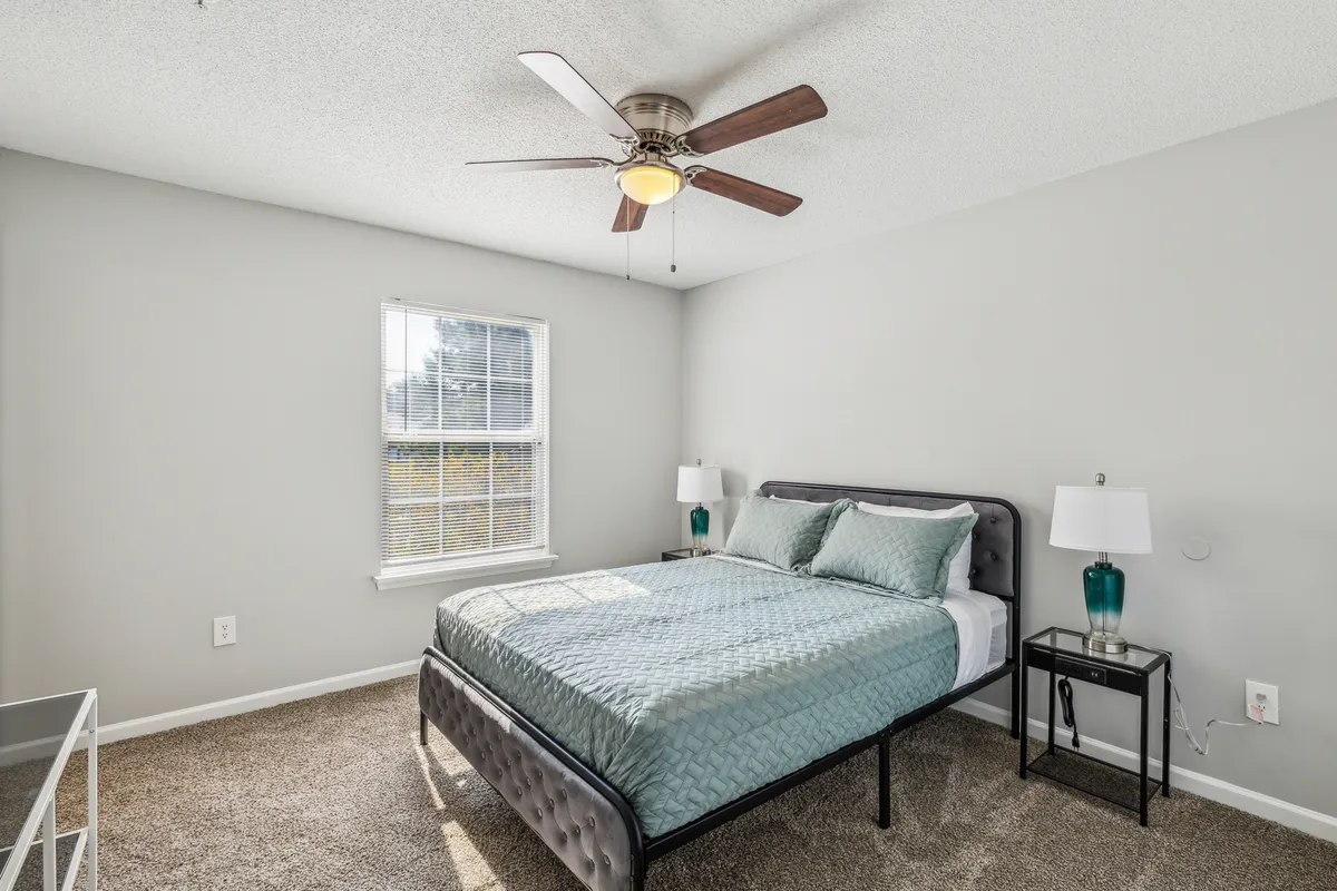 A tranquil bedroom with a cozy bed, sunlit window, and a warm bedside lamp. The soft, neutral décor and natural lighting evoke a peaceful, restful atmosphere, perfect for winding down after a day outdoors.