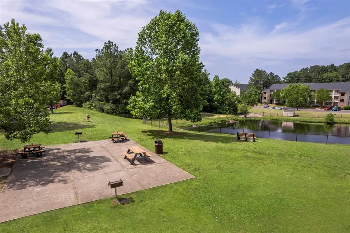 A peaceful outdoor area featuring picnic tables beside a tranquil pond, surrounded by trees and benches, inviting moments of relaxation or socializing. The scene suggests opportunities for morning walks with coffee or leisurely downtime after work.