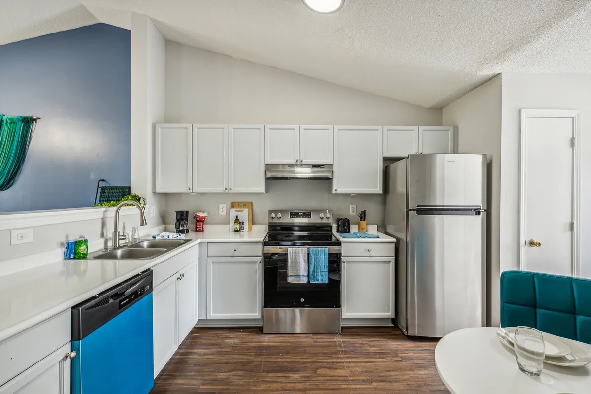 An inviting kitchen scene featuring modern appliances, a generous countertop, and a seamless transition into a cozy dining area. Stools and a dining table are visible, emphasizing both the cooking and eating experience. The overall style is contemporary yet comfortable, designed for gatherings and daily routines.
