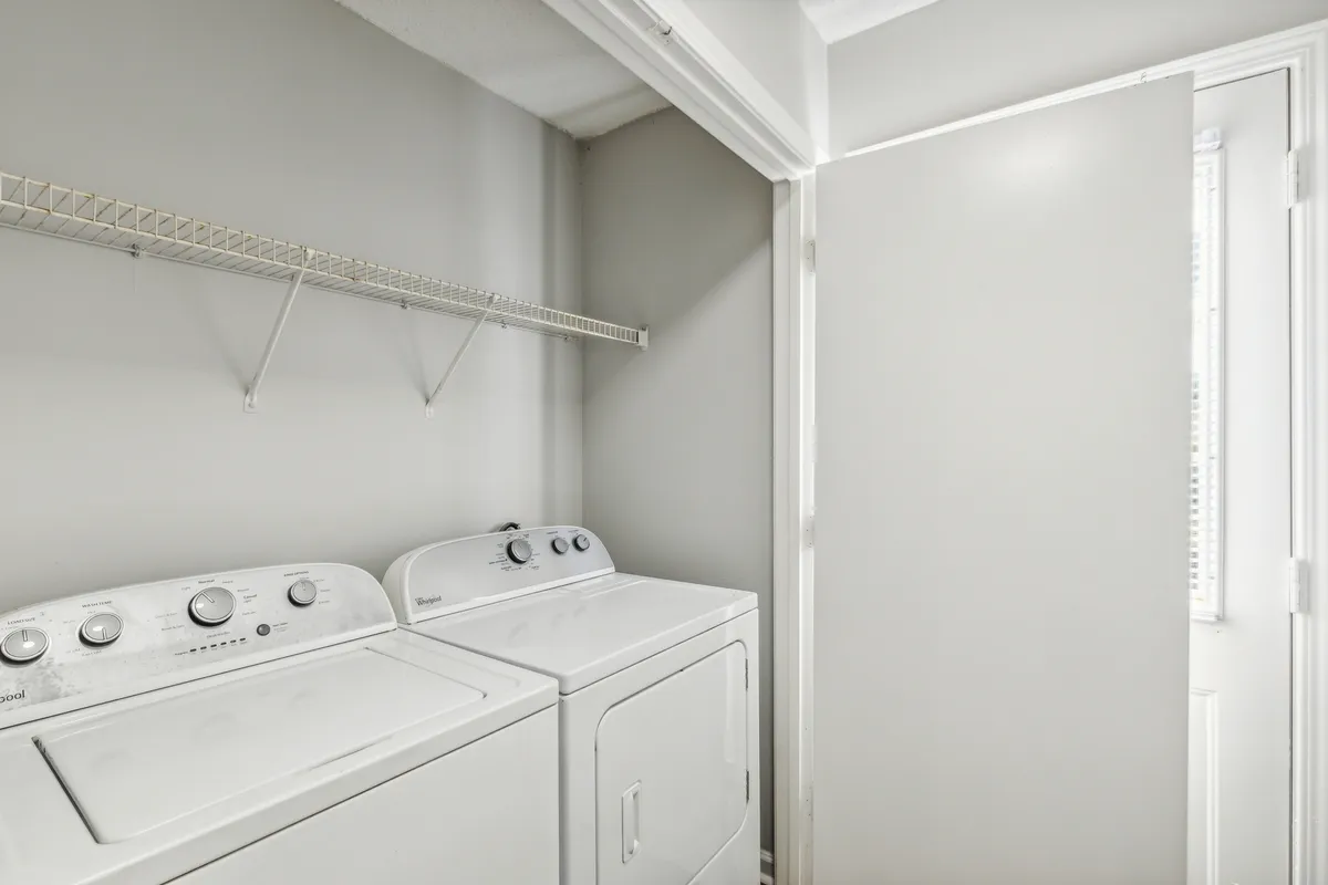 A dedicated laundry room featuring a modern washing machine and dryer, with a shelf above for neatly organized laundry supplies. The space is clean, bright, and clearly designed for ease and efficiency, reflecting the practical aspects of in-unit laundry.