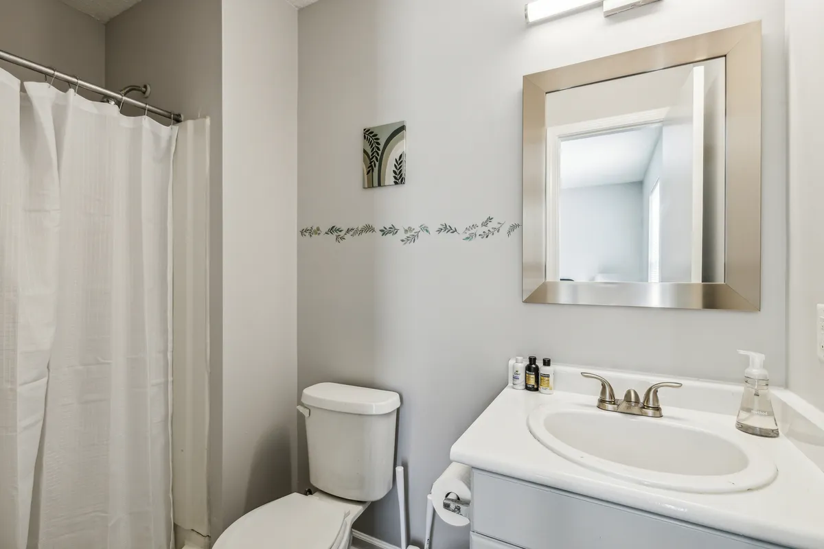 A modern bathroom featuring a large mirror, sleek sink, and a softly patterned shower curtain. The space is bright, clean, and designed for both refreshing morning routines and relaxing evening baths.