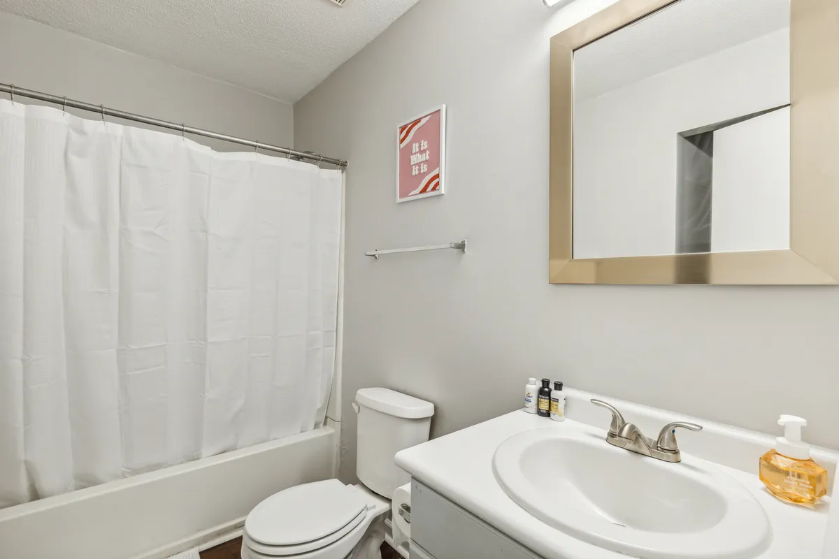A modern, refreshing bathroom with a vanity and sink, large mirror, framed wall art, a bathtub, and a toilet. The space is tidy and soothing, perfect for self-care and relaxation.