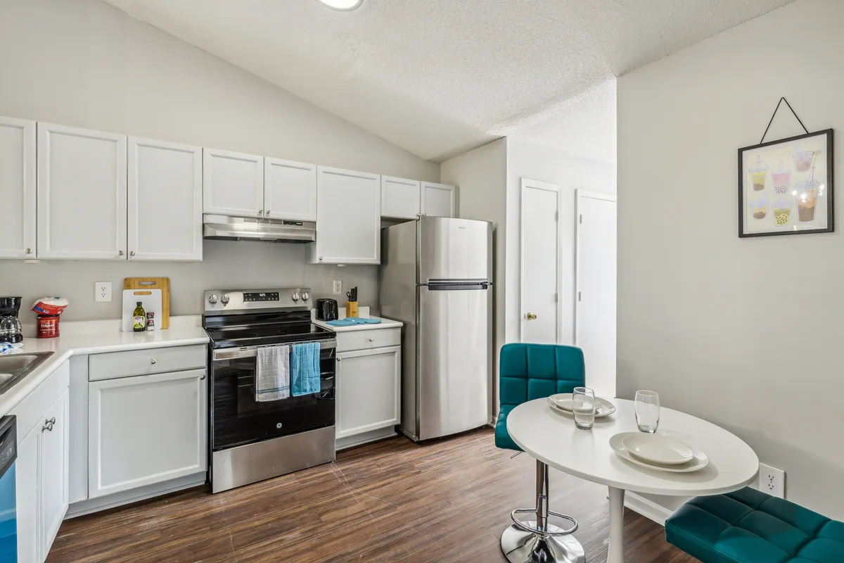 A bright, modern kitchen and dining space featuring colorful chairs around a table, sleek kitchen appliances, and an overall cozy, welcoming vibe. The layout is open, encouraging conversation and togetherness during meals or meal prep.